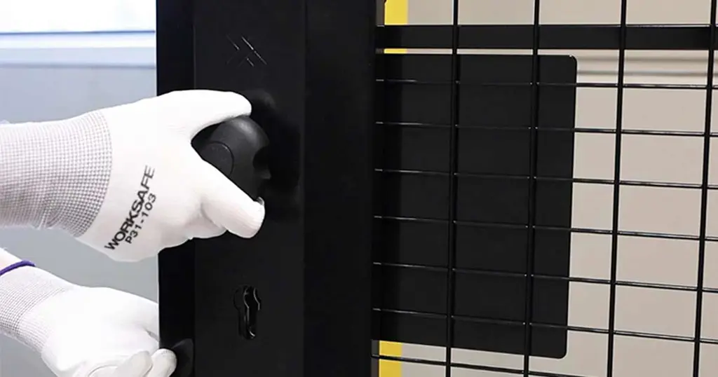 Hand som håller en cylinderformad nödöppningsknapp monterad på en svart nätpanel 